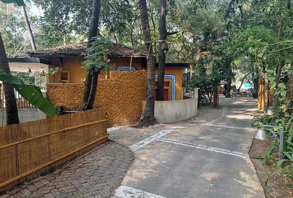 গাছপালা ঘেরা একটি মাটির বাড়ির ছবি, যার সামনে বাঁশের বেড়া এবং একটি হাঁটার রাস্তা দেখা যাচ্ছে।